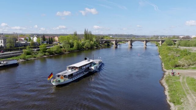 Aerial view of a paddle steamer on the Elbe river near Pirna, featuring the historic city bridge under a blue sky with light clouds.