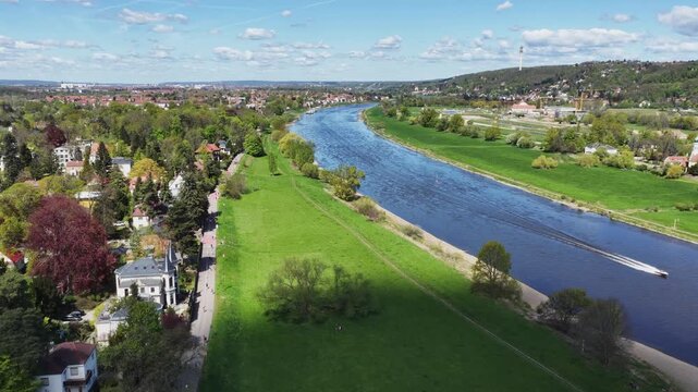 Aerial panorama of the Elbe river near Pirna featuring green meadows, residential areas, and forested hills under a bright blue spring sky.