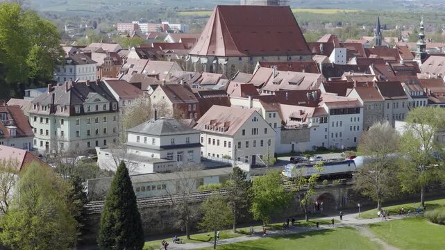 View of Pirna's old town featuring St. Mary's Church and a passing train on the tracks in the foreground during sunny spring weather.