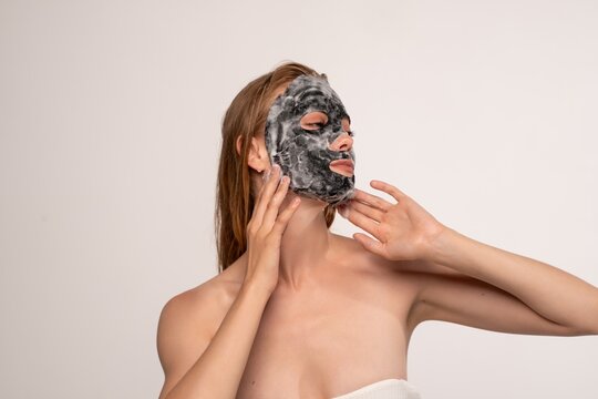 Young woman applying activated charcoal bubble sheet mask for detoxifying facial skincare routine