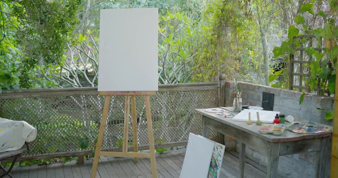 Camera is panning right, shifting wooden easel with blank canvas left, revealing art table on deck