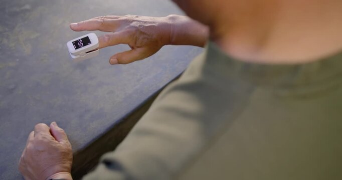 Senior Asian man clipping finger oximeter and adjusting at counter, monitoring readings, copy space