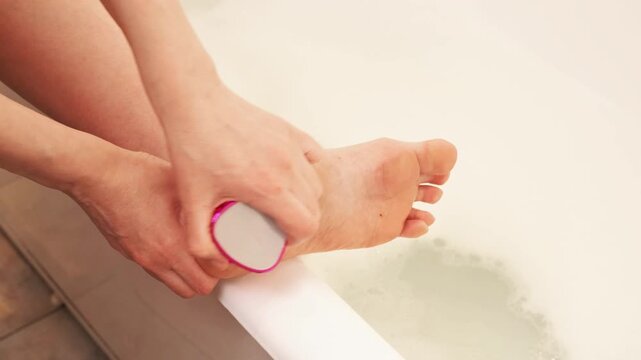 Close up of female hands cleaning heel with pink mechanical file. Home spa and foot care routine for smooth skin preparation