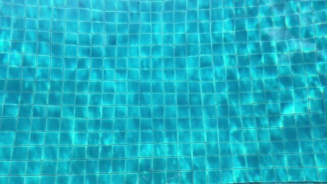 Video of blue pool water with tiled floor and sunlight ripples forming abstract texture, clear and refreshing summer background