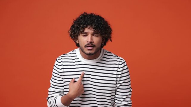 Young Indian man wear striped sweatshirt casual clothes look camera pointing fingers himself ask say who me no thanks i do not need it isolated on plain orange red background studio. Lifestyle concept
