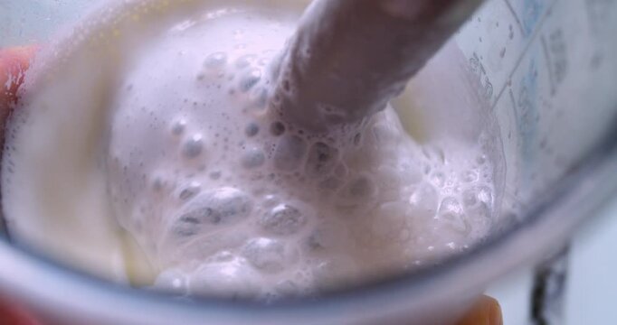 The process of making a milkshake. A mixer froths milk in a plastic cup. Close-up shot from above.