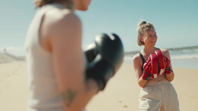 Female boxing coach training with athlete on sunny beach