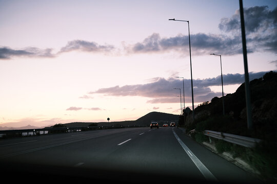 Driving on a coastal highway at dusk with streetlights illuminating the road