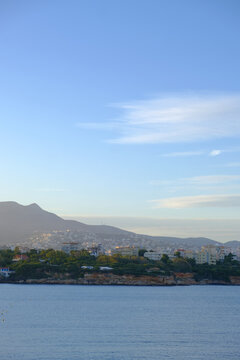Coastal city skyline with mountains and blue sea under a clear sky