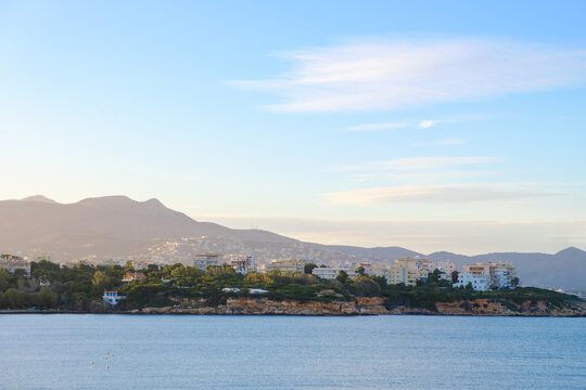Coastal town with modern buildings nestled against rolling hills under a clear sky