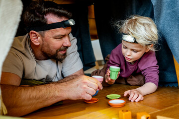 Dad and child building and playing in cozy blanket fort.