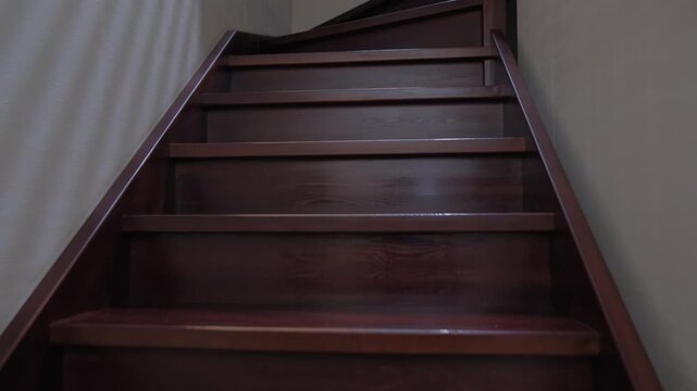 View of wooden stairs leading to the upper floor in a house with soft lighting and plain walls in the background