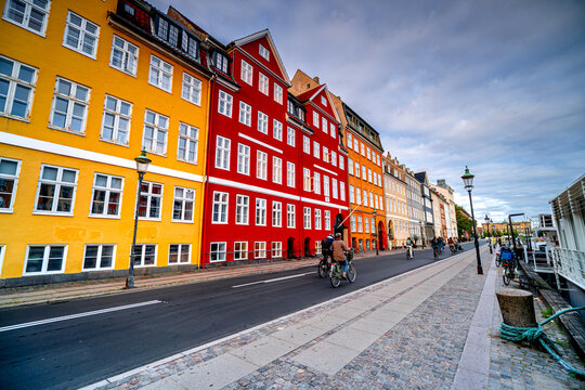 People ride bicycles on colorful street in Danish city Copenhagen in the morning, Denmark, Nyhavn, Indre By district. Life in Scandinavian city.