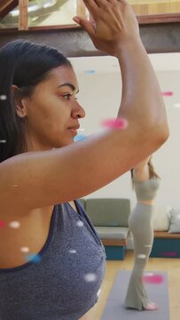 Vertical video: Foreground woman inhaling moving into eagle arms during yoga, mate mirroring on mat