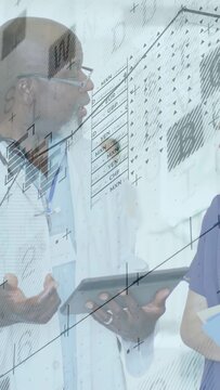 Vertical video: Senior doctor tilting tablet, explaining patient data while nurse checking charts
