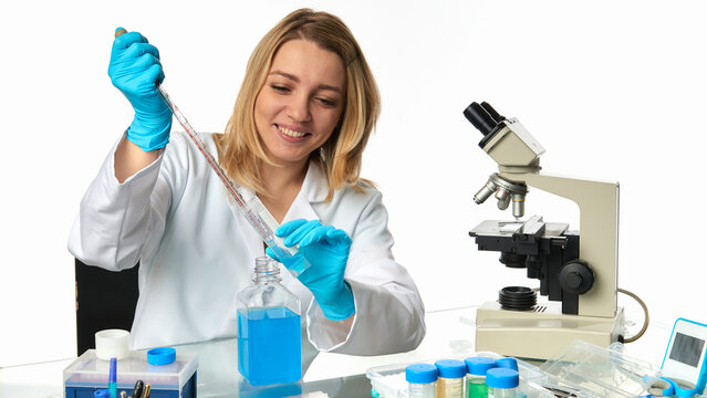 Young european female scientist using  pipette and reagent bottle beside compound microscope