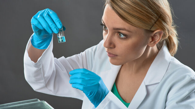 Young european female scientist examining microcentrifuge tube with cultured cells under lab light