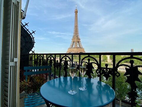 View of the Eiffel Tower from an apartment balcony with two champagne flutes on a table in Paris