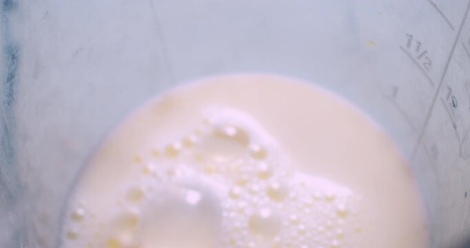 The process of making a milkshake. A mixer froths milk in a plastic cup. Close-up shot from above.