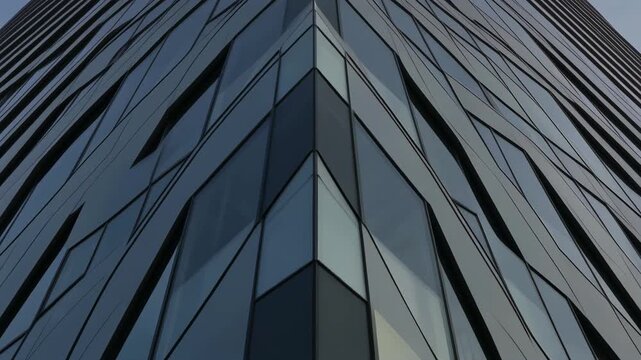 Low-angle view of a modern glass-clad building corner with angular geometry and reflective blue-gray panels, dramatic converging perspective