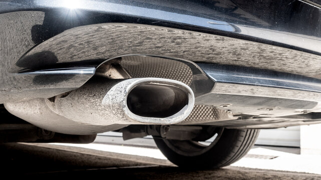Close-up of a car exhaust pipe and muffler under the rear bumper - CO2 emissions and internal combustion vehicles pollution concept