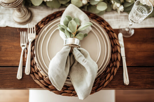 The table is set for a wedding with plates, folded linen napkins, and greenery as accents. Glasses of water sit next to each place setting in a bright indoor setting