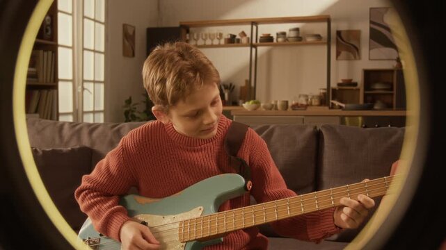 Front view of Caucasian young boy playing electric guitar and recording video for social media, shot framed with ring light lamp with copy space Great for personal branding or creator services