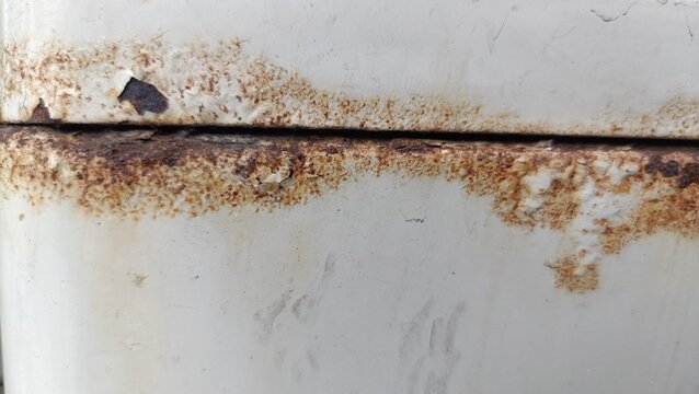 A close-up photo of rusty corrosion on a worn metal surface with visible oxidation and decay marks.