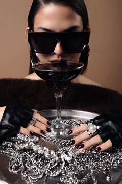 Portrait of a cool woman in sunglasses drinking a cocktail on a tray with assorted jewellery