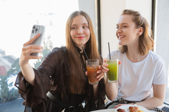 Two smiling young women sitting in a cafe taking a selfie while enjoying iced matcha latte and espresso tonic drinks