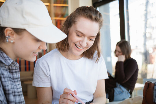 Two smiling young women sitting in a cafe laughing and working together on a creative project