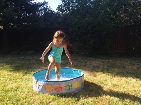 Happy girl in a swimming costume playing in an Inflatable paddling Pool on a summer day