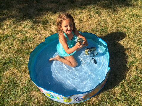 Overhead view of a smiling girl in a swimming costume sitting in an Inflatable paddling Pool on a summer day