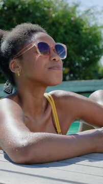 Vertical video: Smiling thirsty woman in yellow top lifting glass, sipping, leaning to man at pool