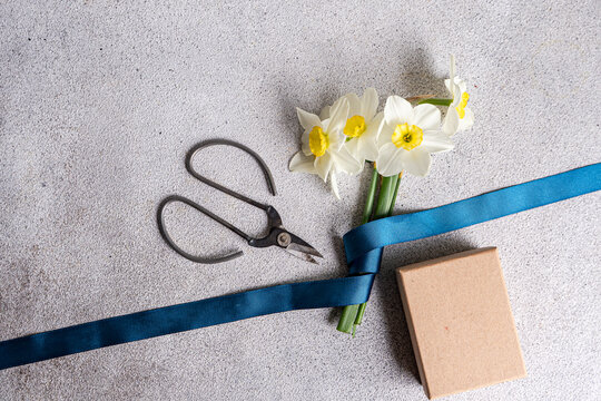 Overhead view of a cardboard Gift box on a table with a pair of scissors and a bunch of fresh daffodils tied with a ribbon