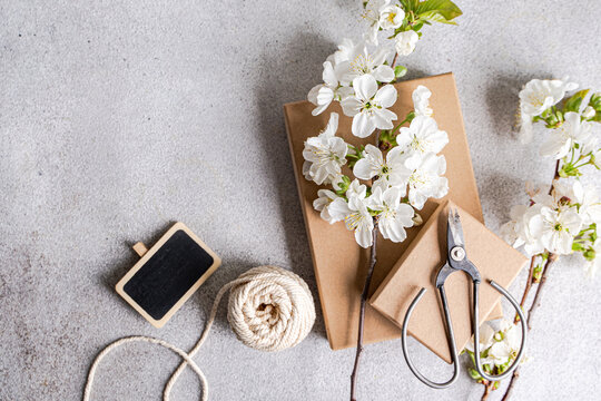 Overhead view of cherry blossom branches on two cardboard gift boxes with a blank chalkboard, string and scissors