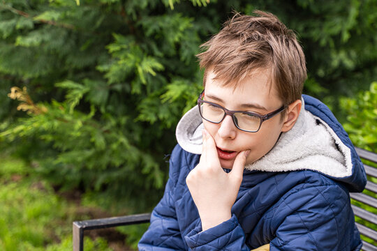 Portrait of a pensive teenage boy sitting on a park bench with his hands on his face