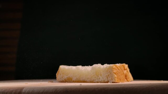 Slices of freshly baked bread falling onto a wooden board against a black background. Concept of baking, culinary arts, and food photography, ideal for use in gastronomy and lifestyle magazines.