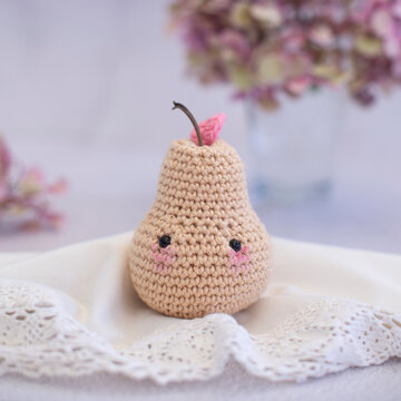 Close-up of a crochet pear toy (Amigurumi) on a table with a vase of hydrangea flowers