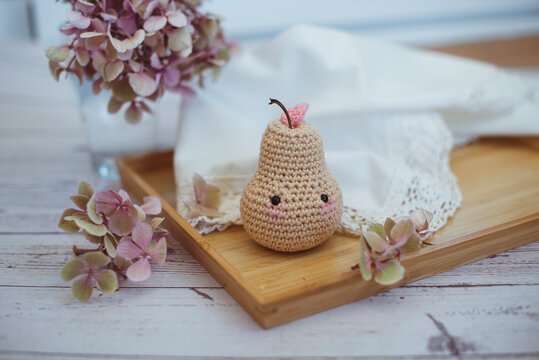 Close-up of a crochet pear toy (Amigurumi) on a wooden tray with a vase of hydrangea flowers