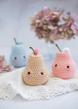 Close-up of three crochet pear toys (Amigurumi) on a table with a vase of hydrangea flowers