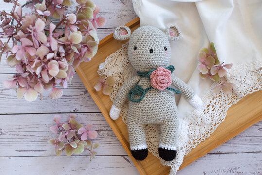 Close-up overhead view of a homemade crochet mouse (Amigurumi) on a tray with hydrangeas on a rustic wooden table