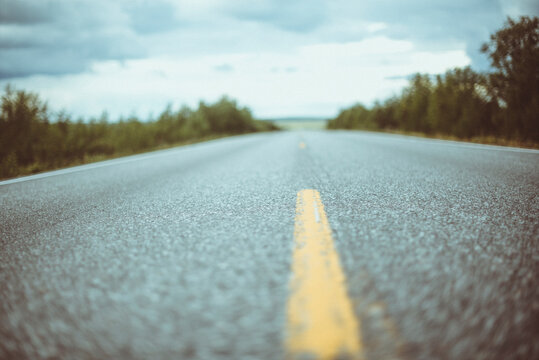 Close-up surface level view of an asphalt road with road markings through a rural landscape on an overcast day, Sweden