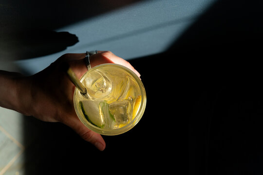 Close-up overhead view of a woman's Hand sitting in the shadows holding a refreshing yuzu melon lemonade drink