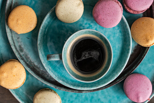 Close-up overhead view of a cup of black coffee with assorted macarons on ceramic crockery on a wooden chopping board and table