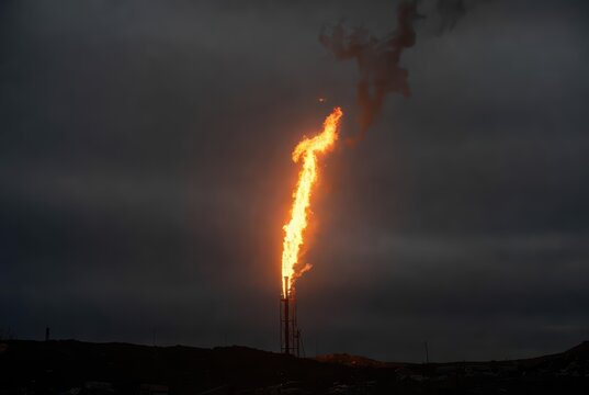 Industrial flare stack burning gas against a dark, cloudy sky at dusk, environmental impact