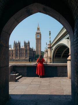 View of a vibrant red-clad figure framed by an archway, gazing across the Thames at Big Ben and Parliament, London, England, United Kingdom.