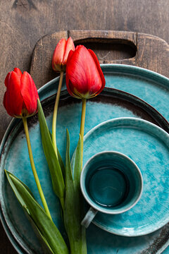 Close-up overhead view of a cup of black coffee and red tulips on ceramic crockery on a wooden chopping board and table