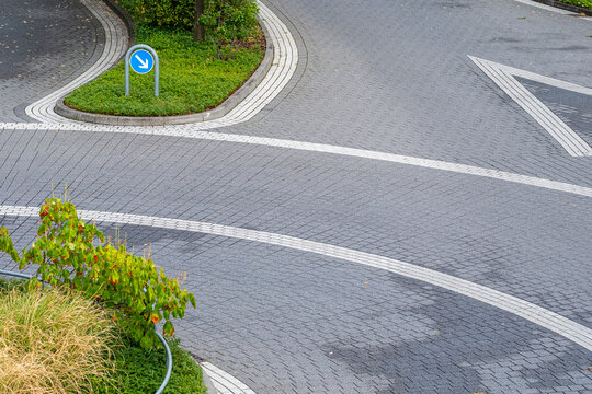 Road markings and pavement curve around an empty urban roundabout where curb signage and minimal infrastructure suggest controlled silence in the city