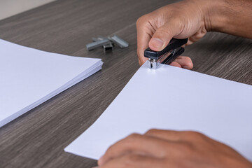 Fototapeta premium Close-up of a person's hand using a stapler to press a stack of white paper an essential office supply